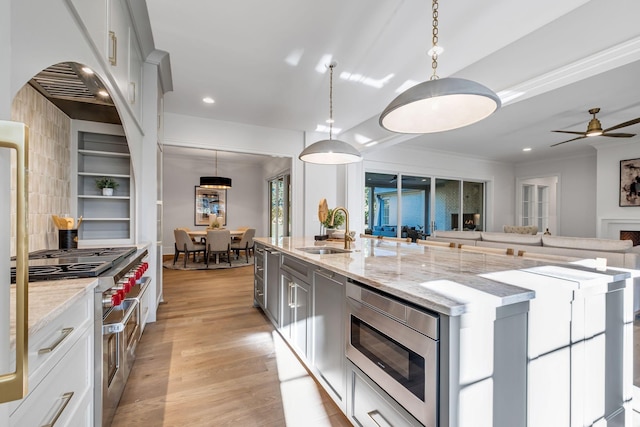 kitchen featuring an island with sink, stainless steel appliances, hanging light fixtures, light stone counters, and sink