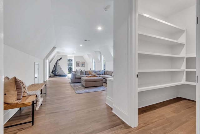 interior space featuring built in shelves, vaulted ceiling, and light wood-type flooring