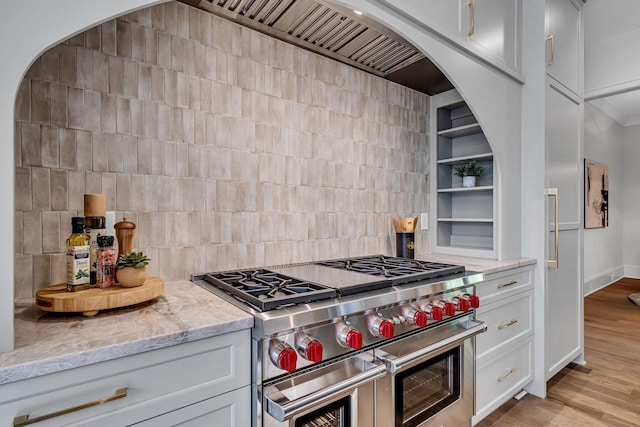 kitchen with backsplash, range with two ovens, light wood-type flooring, white cabinets, and light stone counters