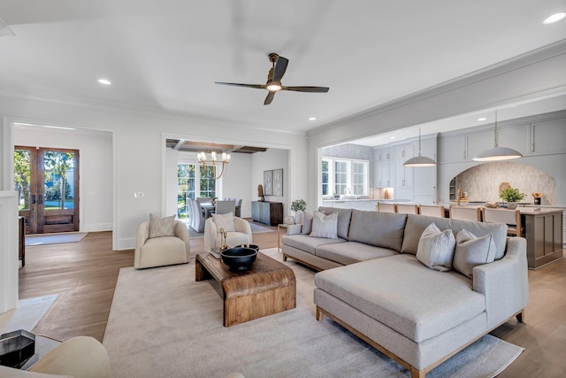 living room featuring ceiling fan with notable chandelier, ornamental molding, and light wood-type flooring