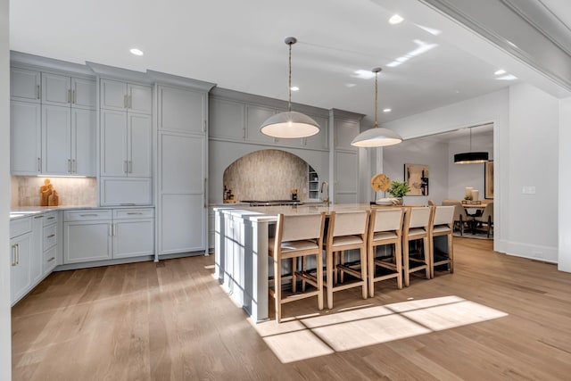 kitchen with tasteful backsplash, gray cabinets, a center island with sink, light wood-type flooring, and a kitchen breakfast bar