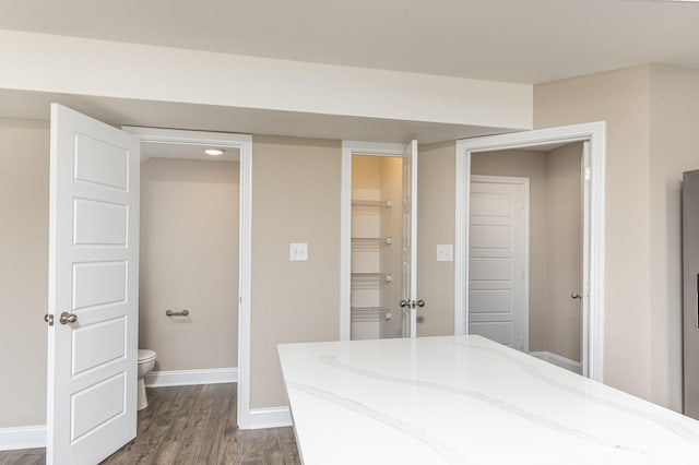 unfurnished bedroom with a spacious closet, ensuite bathroom, a closet, and dark hardwood / wood-style flooring