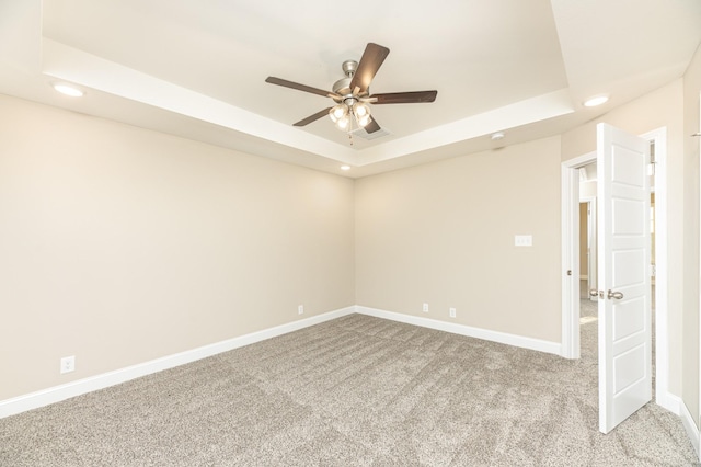 unfurnished room with ceiling fan, light colored carpet, and a tray ceiling