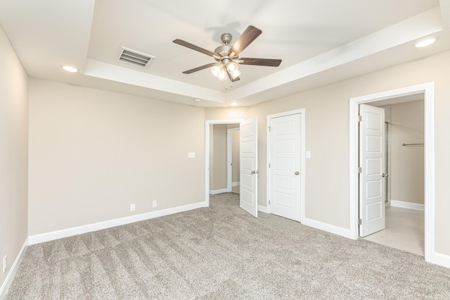 unfurnished bedroom with light carpet, ceiling fan, and a raised ceiling