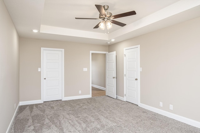 unfurnished bedroom featuring ceiling fan, carpet flooring, and a raised ceiling