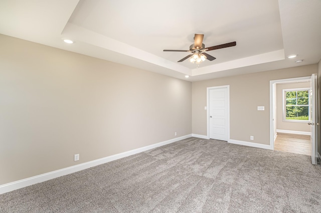 carpeted empty room with ceiling fan and a raised ceiling