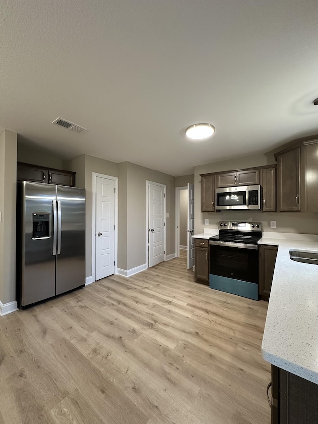 kitchen featuring dark brown cabinetry, light stone counters, light hardwood / wood-style flooring, and appliances with stainless steel finishes