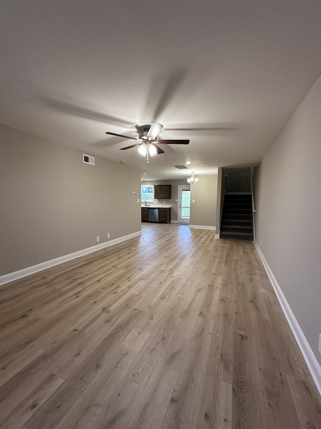 unfurnished living room featuring hardwood / wood-style flooring, ceiling fan with notable chandelier, and a textured ceiling