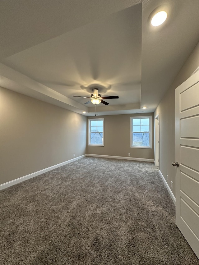 carpeted spare room featuring a raised ceiling and ceiling fan