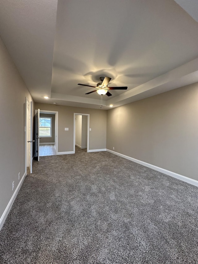 unfurnished bedroom with ceiling fan, a tray ceiling, and dark colored carpet