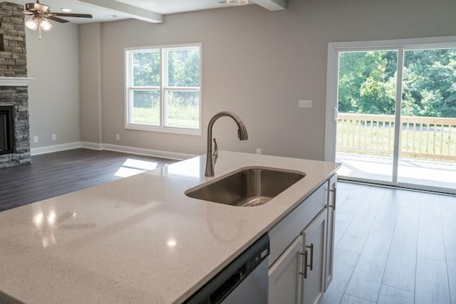 kitchen with beamed ceiling, a fireplace, light stone countertops, a wealth of natural light, and sink