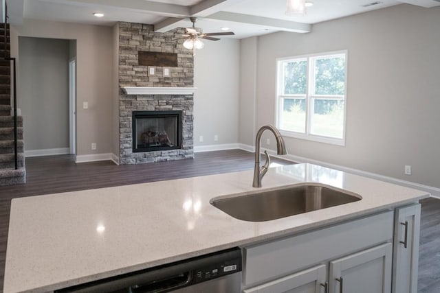 kitchen with beam ceiling, sink, coffered ceiling, a stone fireplace, and light stone counters