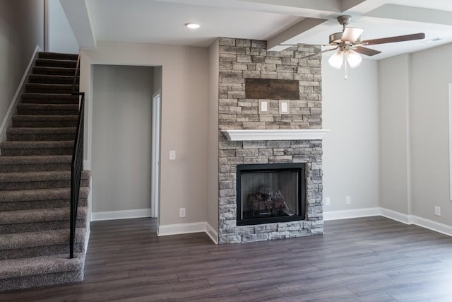 unfurnished living room featuring ceiling fan, dark hardwood / wood-style floors, a stone fireplace, and beamed ceiling