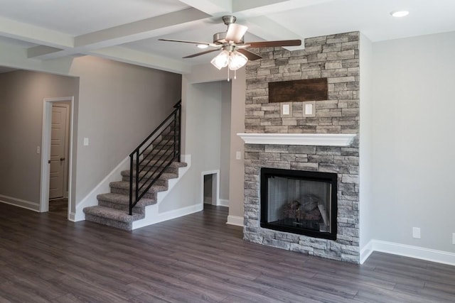 unfurnished living room featuring beam ceiling, ceiling fan, dark hardwood / wood-style floors, and a stone fireplace