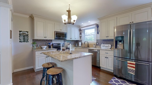 kitchen with appliances with stainless steel finishes, a kitchen island, decorative light fixtures, sink, and light stone counters