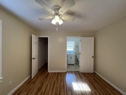 unfurnished bedroom with ceiling fan, ensuite bath, a spacious closet, a closet, and dark hardwood / wood-style flooring