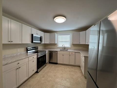 kitchen with light stone countertops, stainless steel appliances, white cabinets, and sink