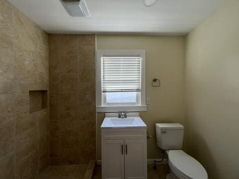 bathroom featuring toilet, vanity, and tiled shower