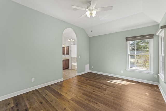 spare room with vaulted ceiling, dark wood-type flooring, and ceiling fan with notable chandelier