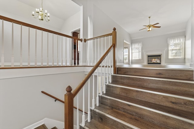 staircase with ceiling fan with notable chandelier and vaulted ceiling