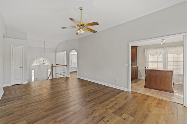 unfurnished living room featuring hardwood / wood-style flooring, plenty of natural light, ceiling fan with notable chandelier, and vaulted ceiling