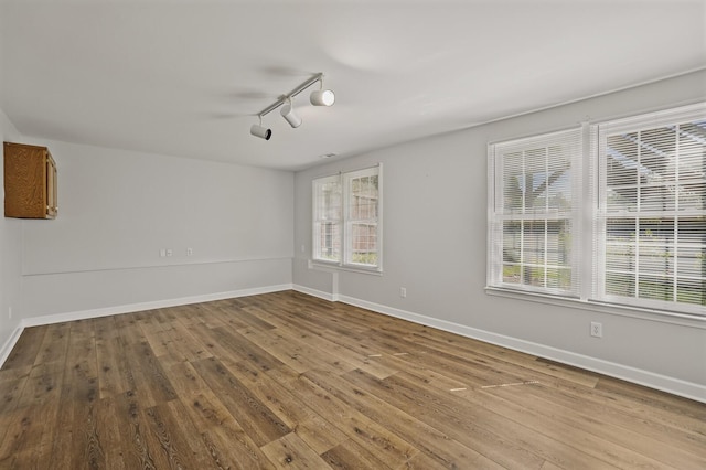 spare room with rail lighting, wood-type flooring, and a healthy amount of sunlight