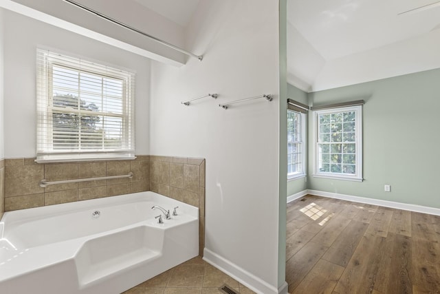 bathroom with a tub to relax in, a healthy amount of sunlight, vaulted ceiling, and hardwood / wood-style floors