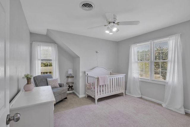 bedroom featuring ceiling fan, light colored carpet, multiple windows, and a nursery area