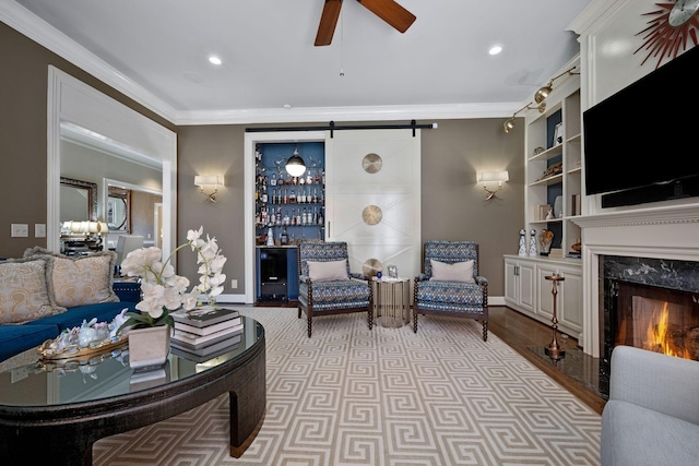 living room with ceiling fan, a barn door, a premium fireplace, built in features, and ornamental molding