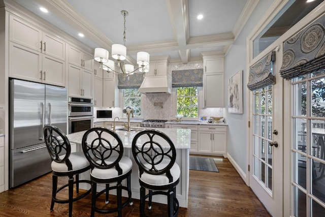 kitchen with white cabinetry, stainless steel appliances, backsplash, a kitchen island with sink, and beam ceiling