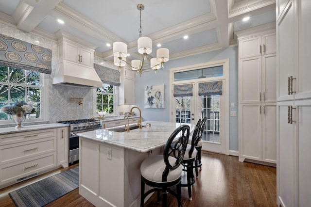 kitchen featuring light stone countertops, high end stainless steel range, white cabinets, an island with sink, and sink