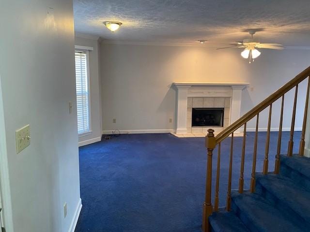 unfurnished living room featuring ceiling fan, a tile fireplace, crown molding, and dark colored carpet