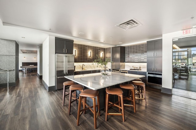 kitchen featuring a kitchen island, a kitchen bar, dark hardwood / wood-style flooring, stainless steel appliances, and backsplash