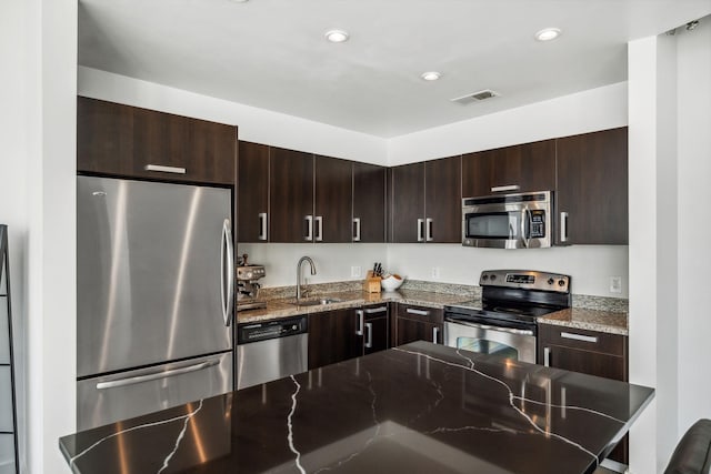 kitchen with stainless steel appliances, dark stone countertops, dark brown cabinets, and sink