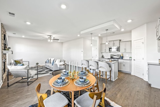 dining area featuring ceiling fan, dark hardwood / wood-style floors, a stone fireplace, and sink