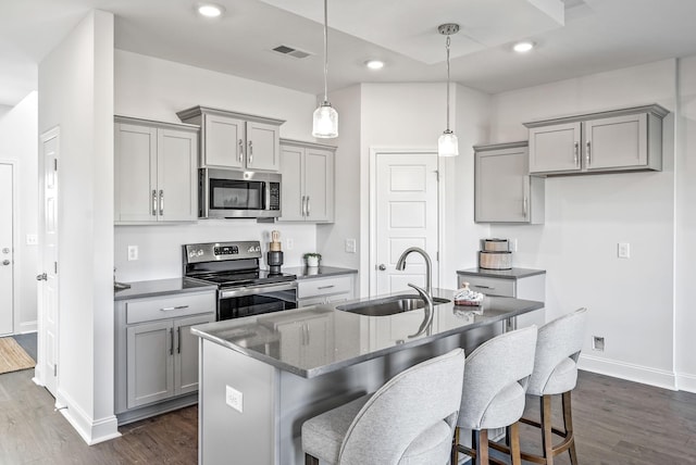 kitchen featuring appliances with stainless steel finishes, sink, hanging light fixtures, gray cabinets, and a kitchen island with sink