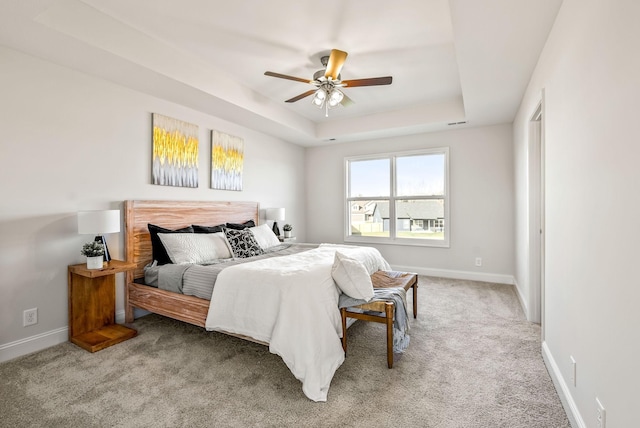 carpeted bedroom with ceiling fan and a tray ceiling