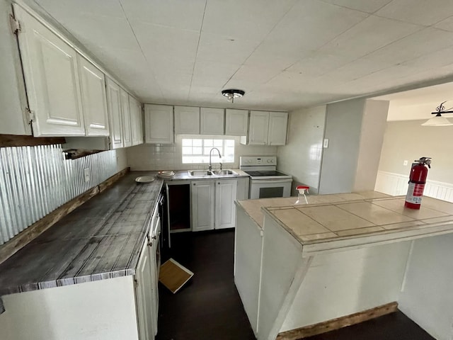 kitchen featuring tile countertops, kitchen peninsula, white electric stove, white cabinets, and sink