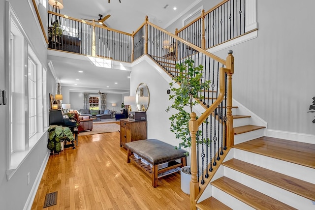 staircase featuring ceiling fan, a towering ceiling, ornamental molding, and hardwood / wood-style floors