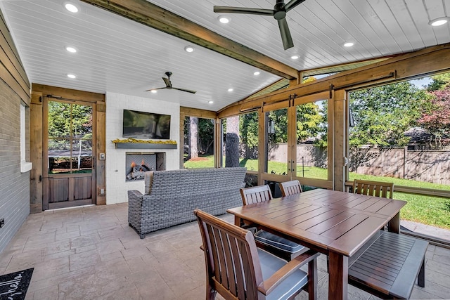 sunroom featuring ceiling fan, a healthy amount of sunlight, lofted ceiling with beams, and a large fireplace