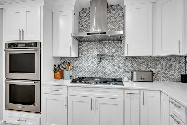 kitchen with decorative backsplash, white cabinetry, wall chimney range hood, and stainless steel appliances