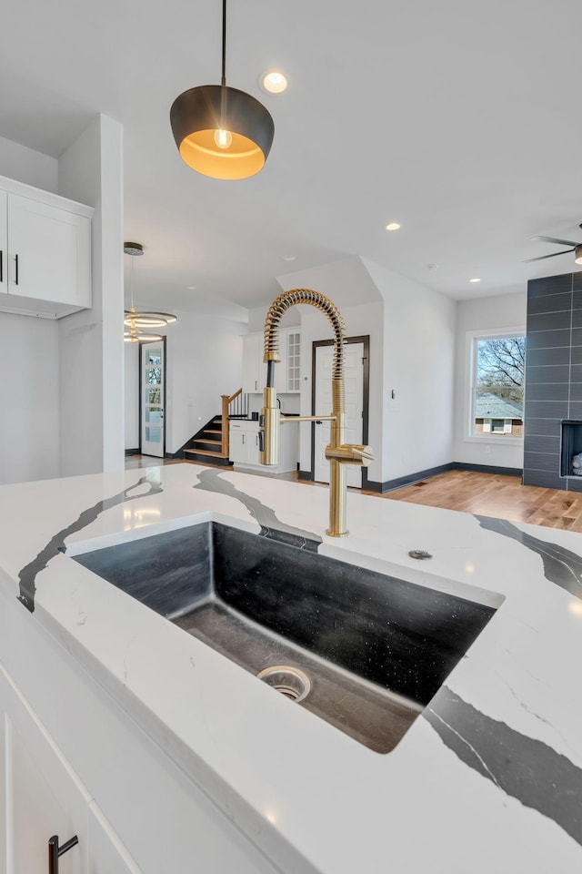 interior details featuring a fireplace, hardwood / wood-style floors, sink, white cabinetry, and hanging light fixtures