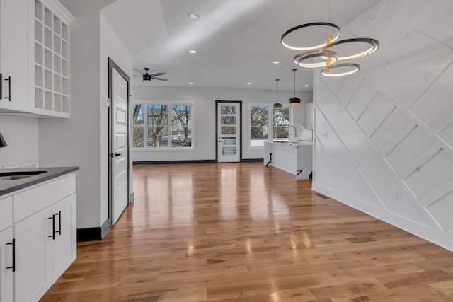 kitchen with ceiling fan with notable chandelier, pendant lighting, white cabinetry, light hardwood / wood-style floors, and sink