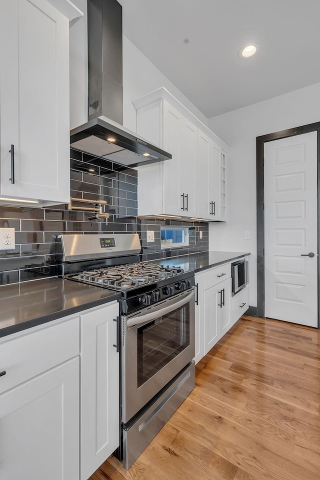 kitchen with stainless steel gas stove, light hardwood / wood-style floors, wall chimney range hood, and white cabinets