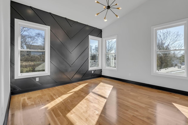 unfurnished room featuring light wood-type flooring, a wealth of natural light, vaulted ceiling, and a notable chandelier