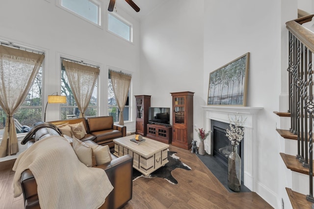 living room with ceiling fan, dark hardwood / wood-style flooring, a premium fireplace, and a high ceiling