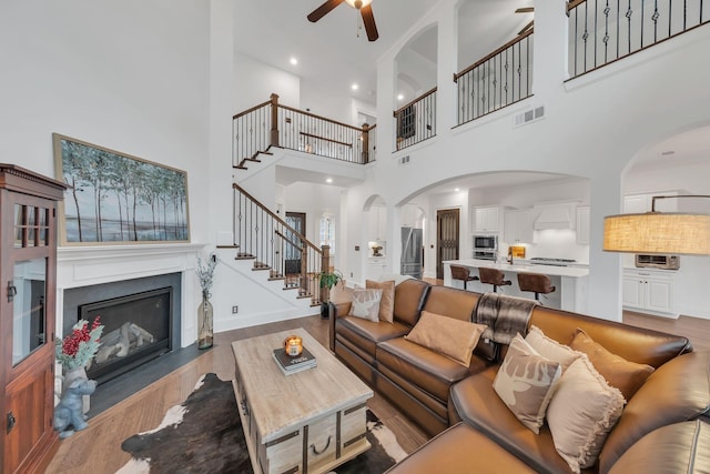 living room with ceiling fan, a high ceiling, and light hardwood / wood-style floors