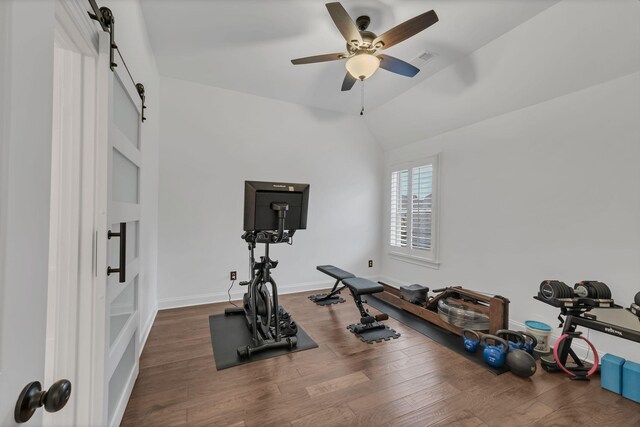 workout area featuring ceiling fan, dark wood-type flooring, a barn door, and vaulted ceiling