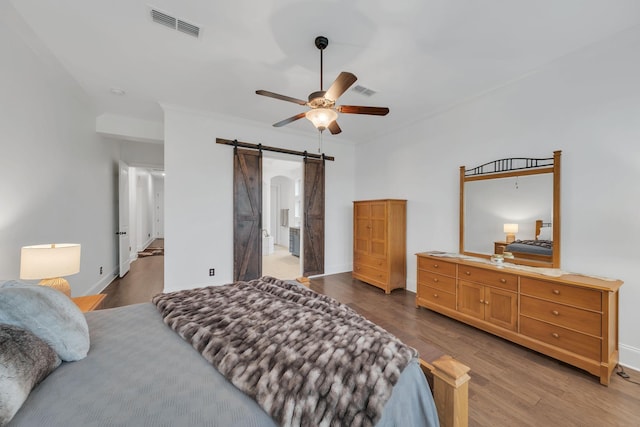 bedroom featuring ensuite bath, dark hardwood / wood-style flooring, ornamental molding, ceiling fan, and a barn door