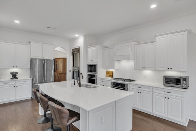 kitchen with decorative backsplash, white cabinetry, a center island with sink, and stainless steel appliances